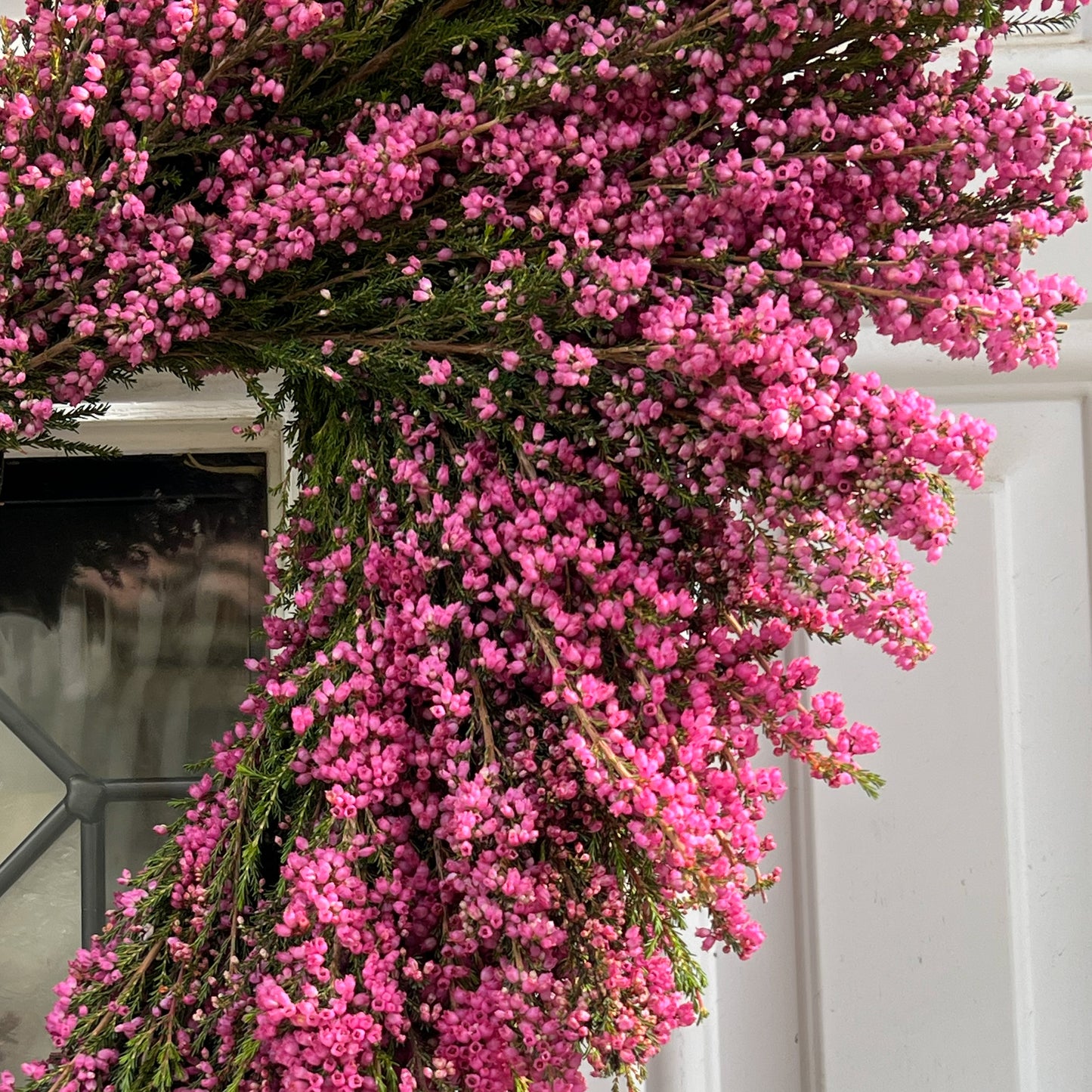 Upper Right Close Up Shot of a Hot Pink Erica Heather Heart Wreath Hung on A White Door