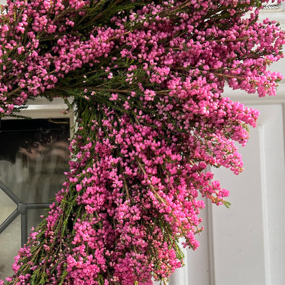 Upper Right Close Up Shot of a Hot Pink Erica Heather Heart Wreath Hung on A White Door